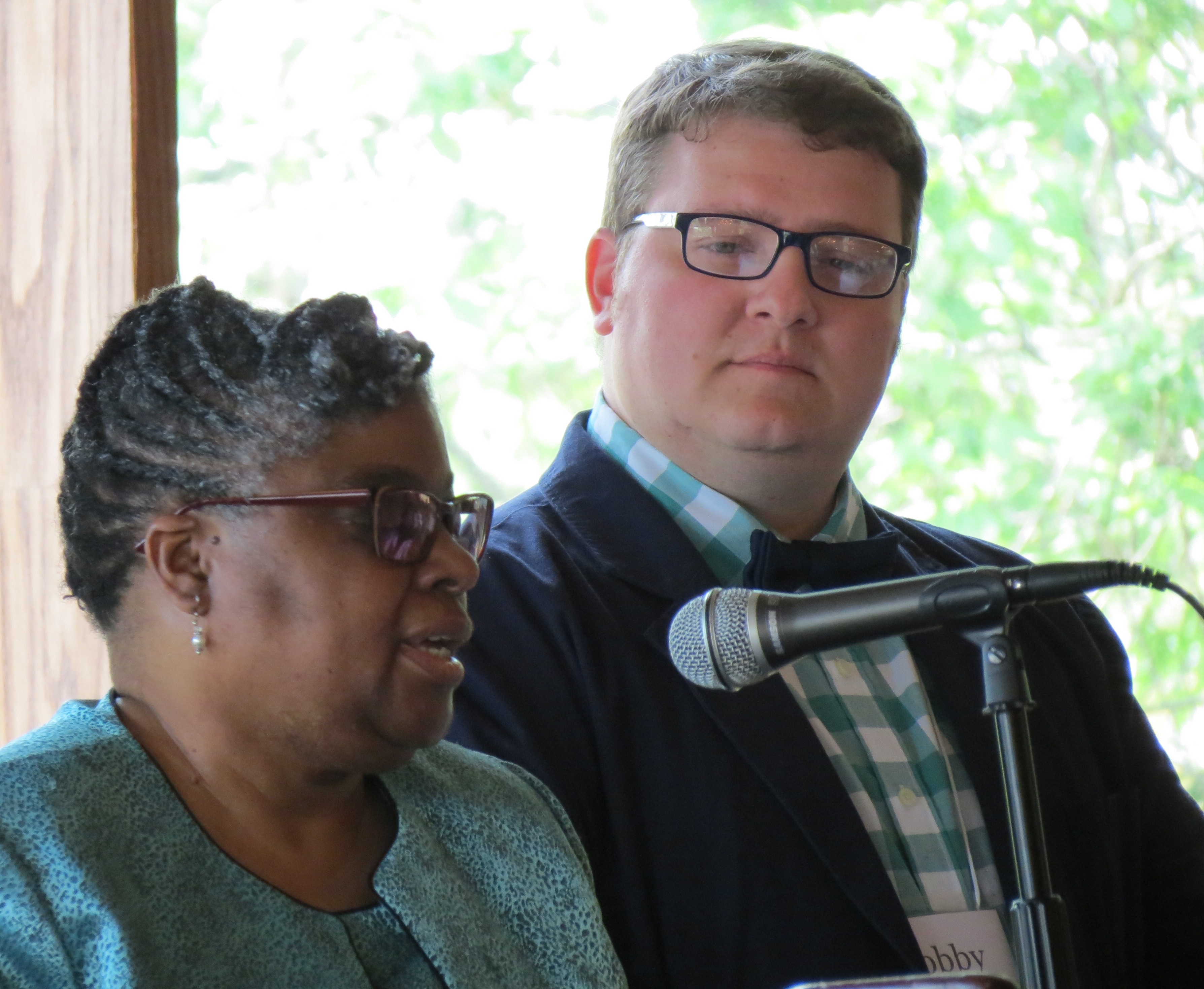 A woman speaking into a microphone, and a man looking at her